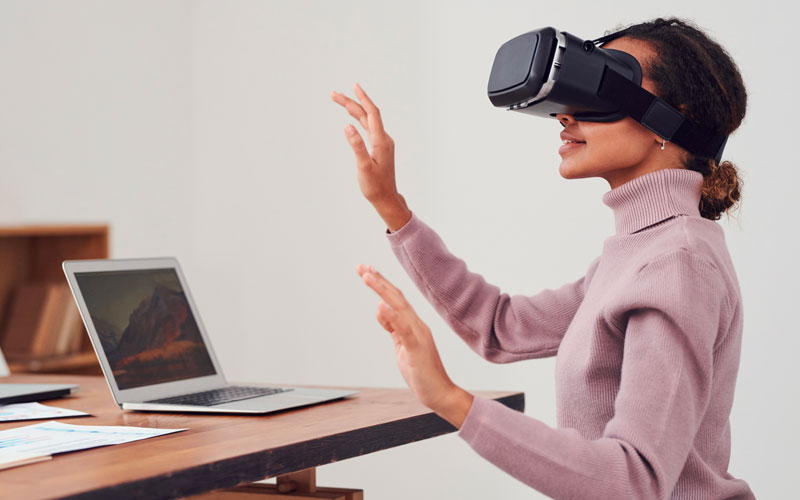 Une femme portant un casque de réalité virtuelle et assise face à un ordinateur