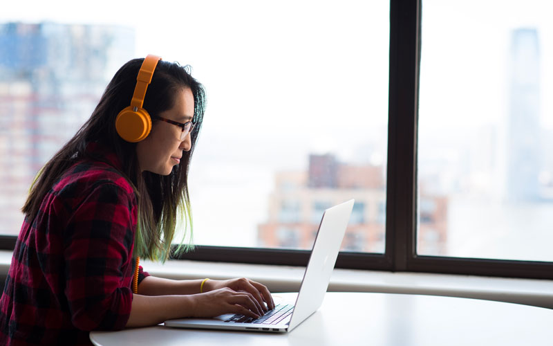 Une femme suit un module e-learning sur un ordinateur, un casque audio sur les oreilles