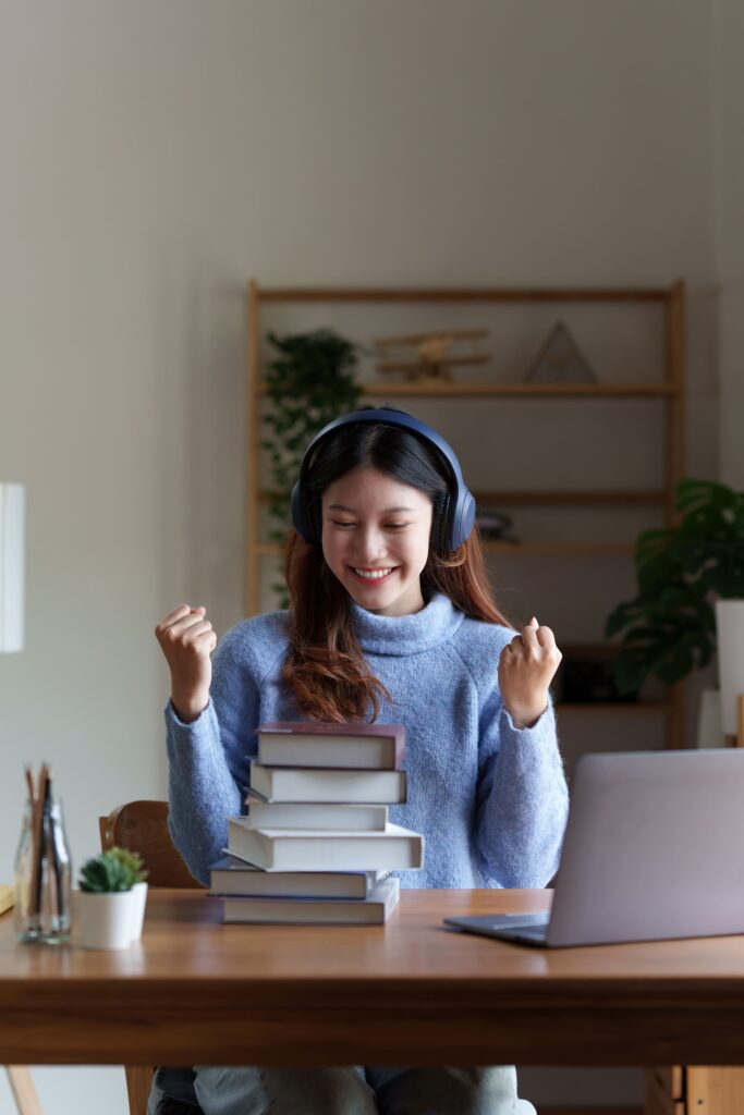 Une femme se réjouit d'apprendre à distance, elle serre les poings de joie face à son ordinateur et une pile de livres