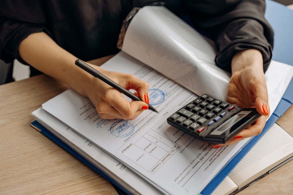Une personne utilise une calculatrice et note des informations dans un cahier : Elle calcule les aides financières e-learning auxquelles elle peut prétendre.