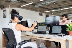 Une femme porte un casque de réalité virtuelle et interagit avec un ordinateur.